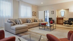 Una sala de estar moderna con un sofá color beige, una mesa de centro de vidrio y detalles en rojo.