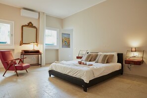A bedroom with a bed, a chair, a desk, a mirror, and a wall-mounted lamp.