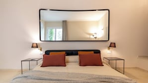 Un dormitorio ordenado con una cama grande, dos mesitas de noche y un espejo fijado a la pared.