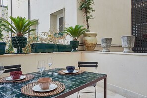 A dining table set with plates, bowls, and wine glasses, surrounded by chairs and potted plants.