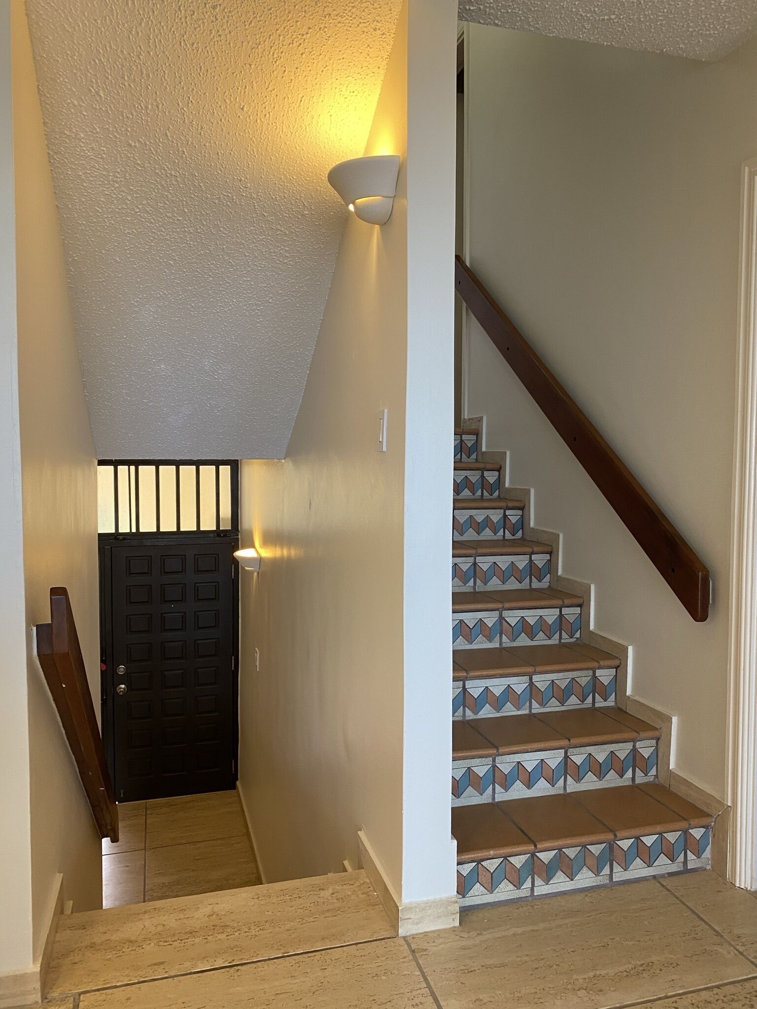 A staircase with patterned tiles, a black door, and a light fixture on the wall.