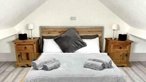 A bedroom with a sloped ceiling, a wooden bed frame, two nightstands, and a bedside table with lamps.
