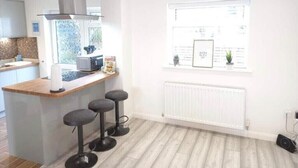 A modern kitchen with a central island, bar stools, a window with a view, and a white radiator.