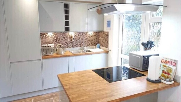 A modern kitchen with white cabinets, a wooden countertop, and a built-in stove.