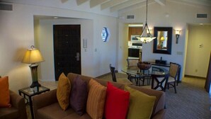 A living room with a brown sofa, a glass coffee table, and a lamp. There is a dining area with a round table and chairs. - Scottsdale Camelback Resort Spacious 2BR Condo with Picnic Area (Scottsdale)
