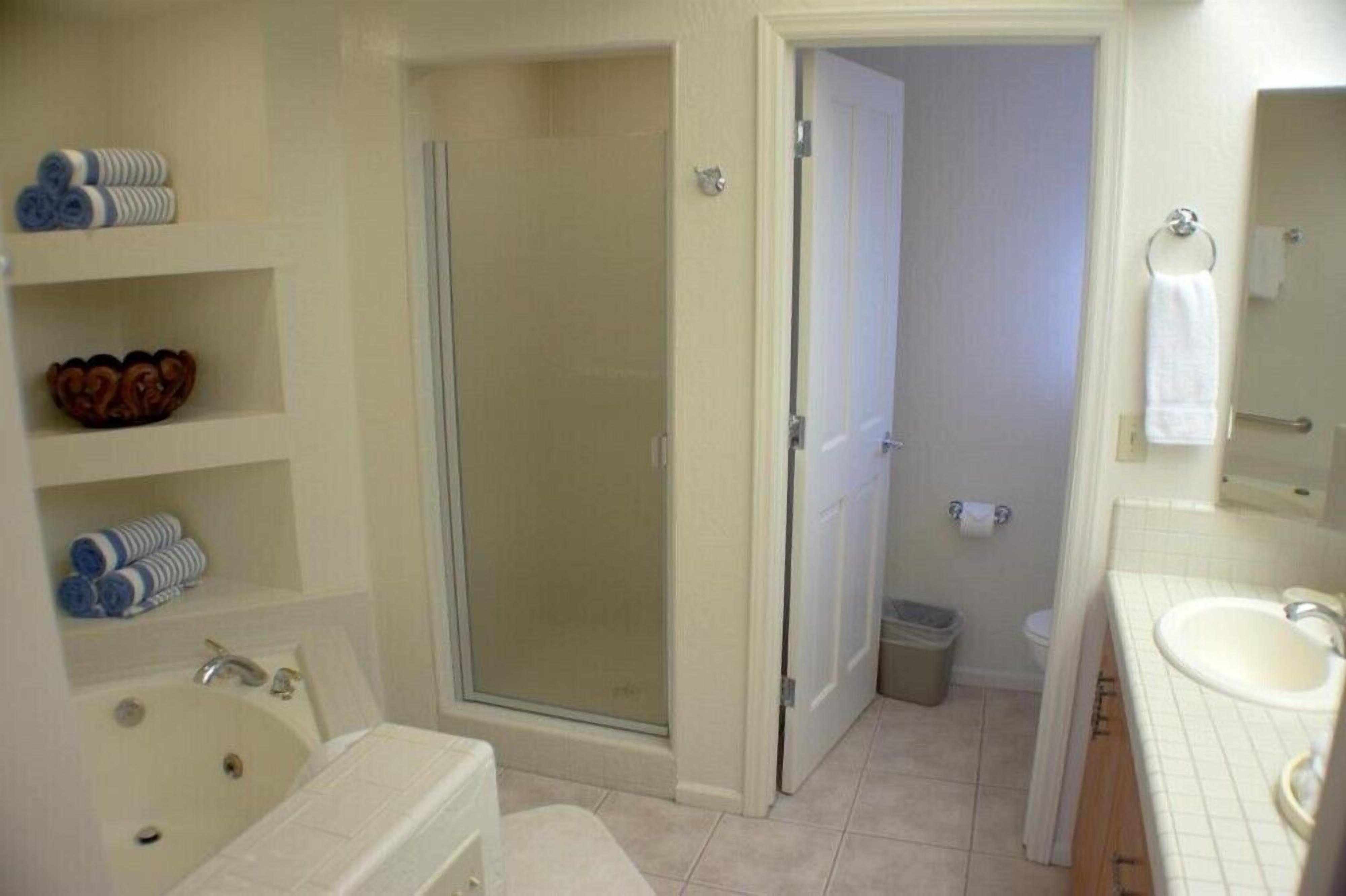 A bathroom with a shower, toilet, sink, and shelves with towels.