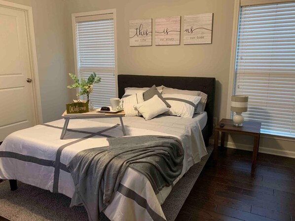A bedroom with a bed, bedside tables, a nightstand, a lamp, and a window with blinds.