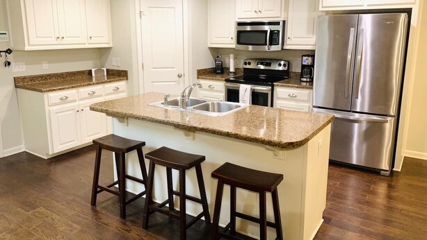 A kitchen with white cabinets, a granite countertop, a stainless steel refrigerator, and a microwave. - Peaceful 3BR/2BA Hidden Lake Home Near ACOM w/WiFi (Dothan)