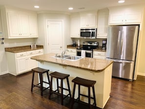 A kitchen with white cabinets, a granite countertop, a stainless steel refrigerator, and a microwave.