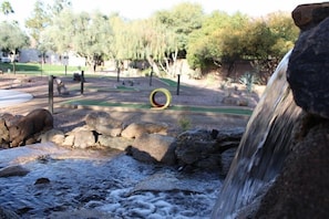 Un entorno de parque natural con cascada, rocas y una estructura de juego circular.