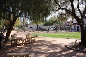 Un patio al aire libre con sillas y una mesa de madera, rodeado de árboles y un jardín ajardinado.