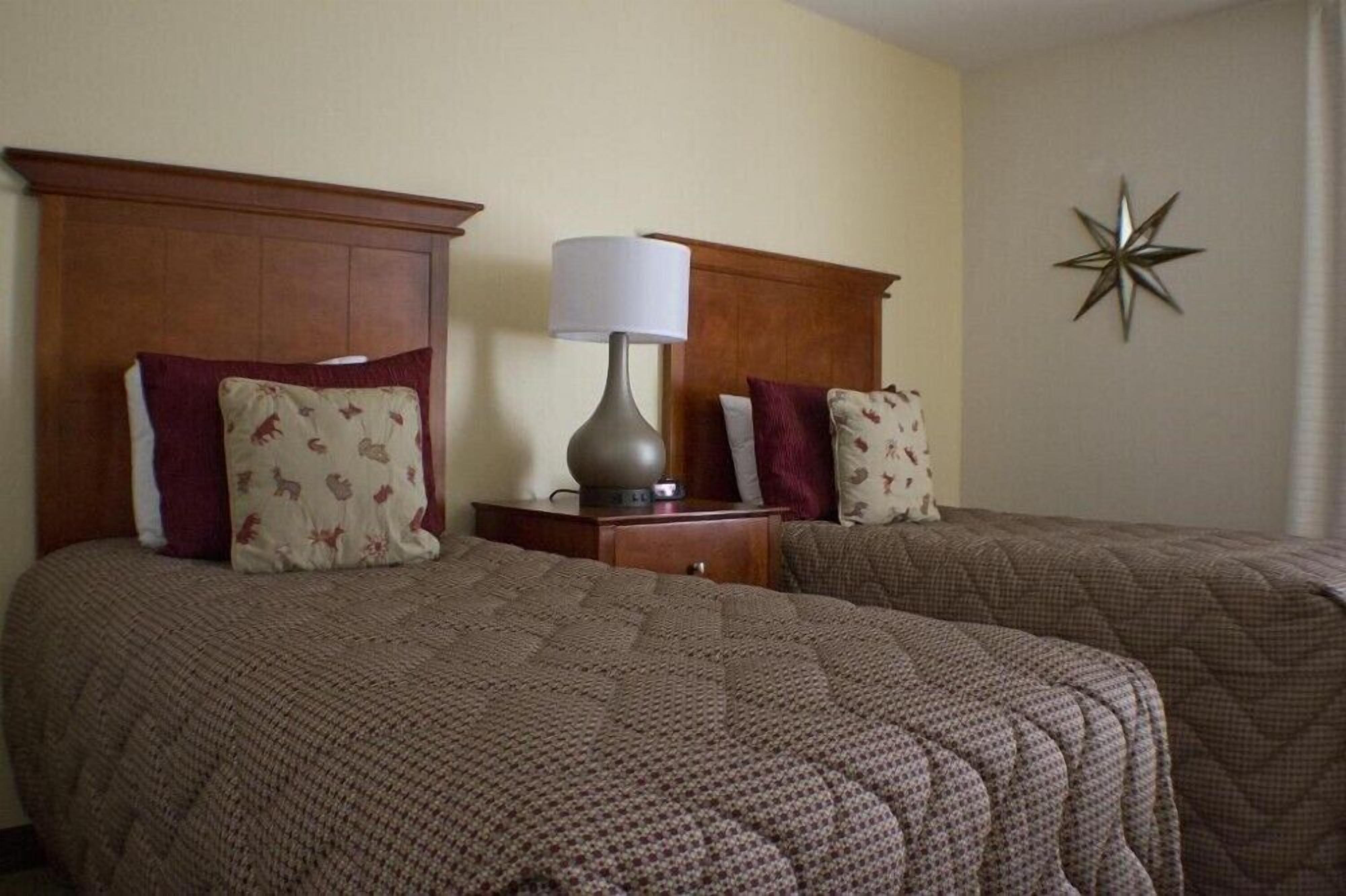 Une chambre d’hôtel avec deux lits, chacun doté d’une tête de lit en bois, d’une table de chevet avec une lampe et d’une étoile décorative sur le mur.