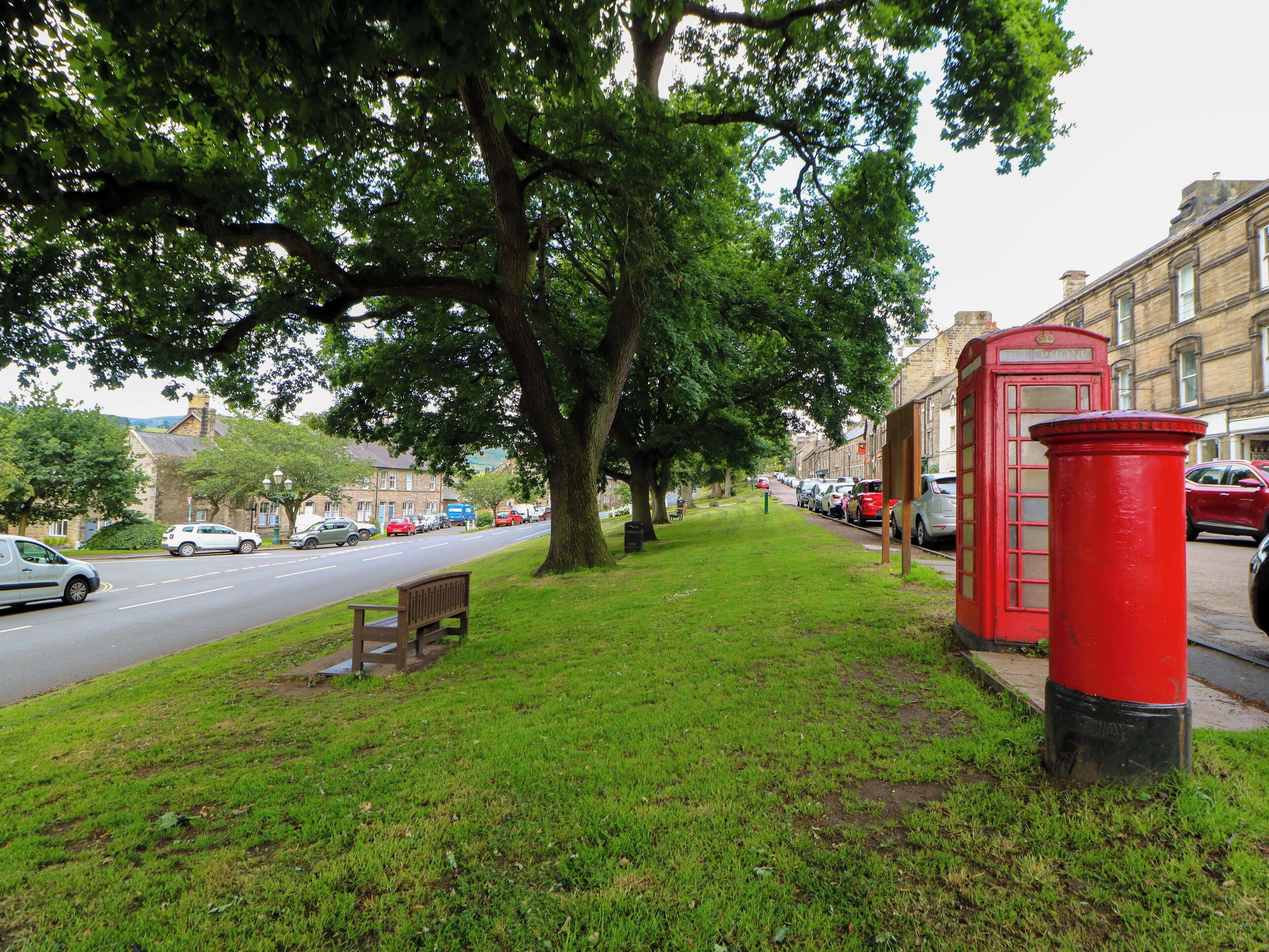 A street with parked cars, a red telephone booth, and a bench under a tree.