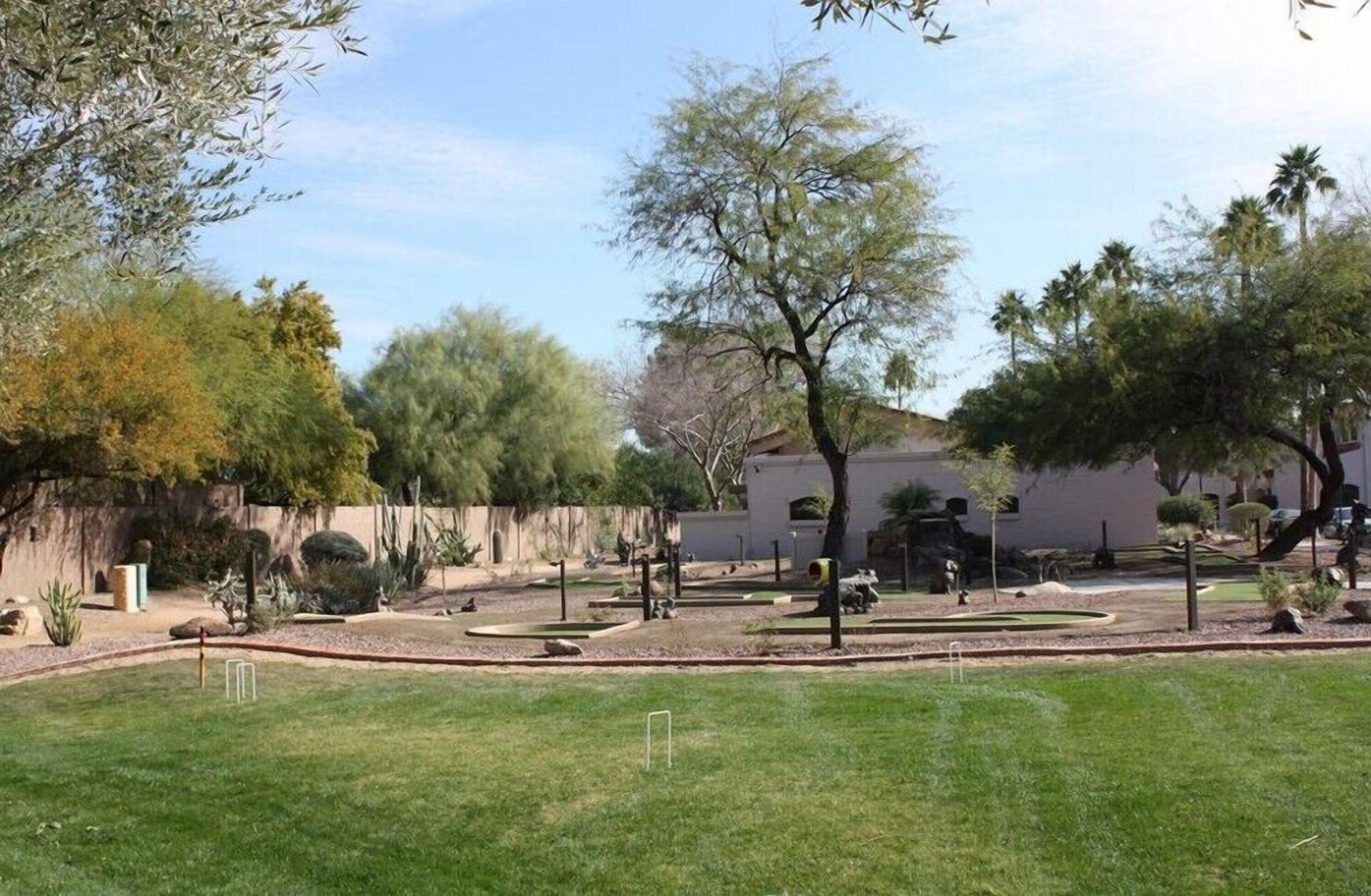 A landscaped garden with various plants and trees, a white building in the background, and a clear sky.
