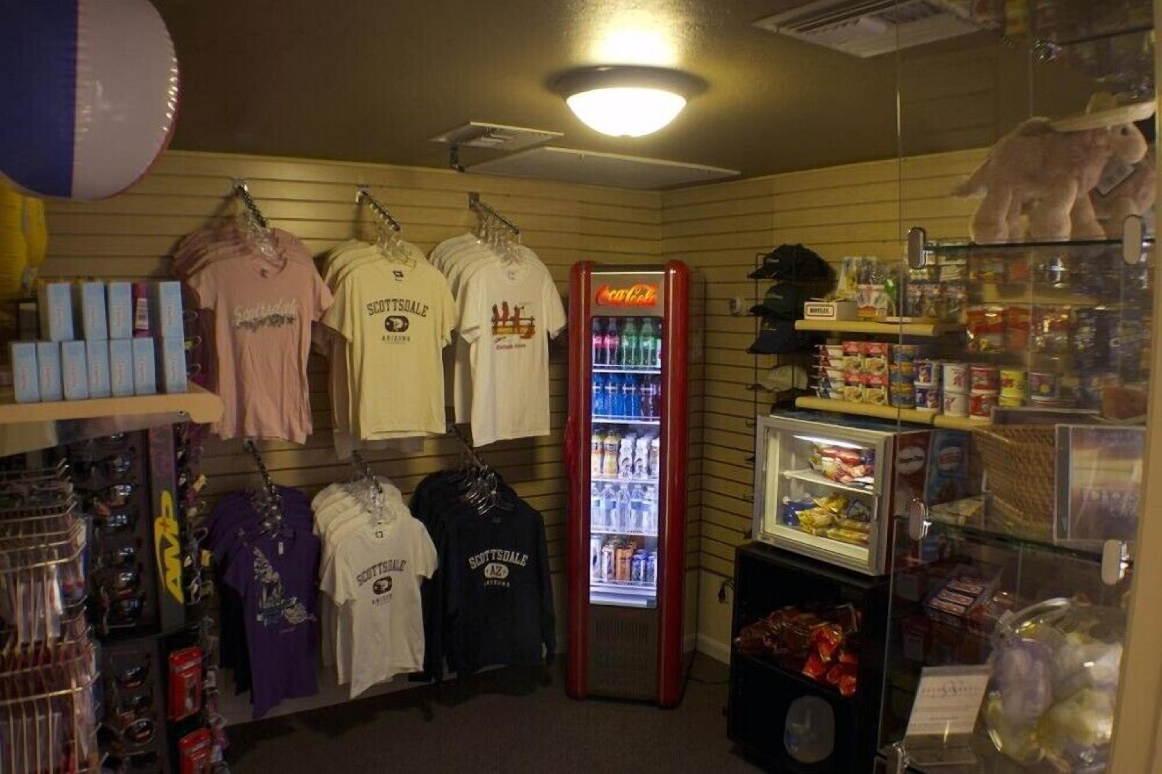 Un espacio comercial con percheros de ropa, un refrigerador de Coca-Cola y varios productos envasados.
