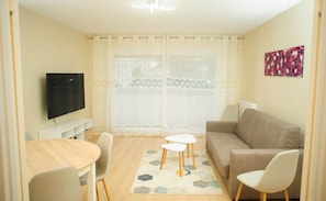 A living room with a beige sofa, a TV, a dining table with chairs, and a patterned rug.