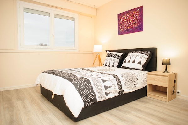 A bedroom with a bed, bedside lamps, a window, and a wall art piece.