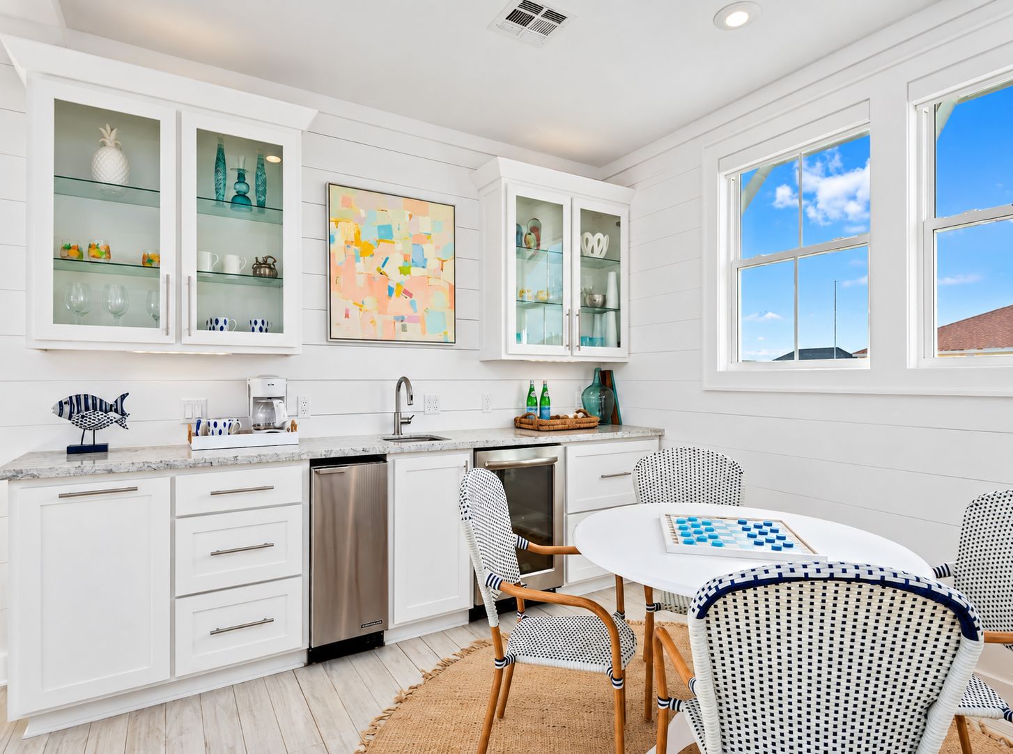 A modern kitchen with white cabinetry, a dishwasher, and a dining area with wicker chairs and a table.
