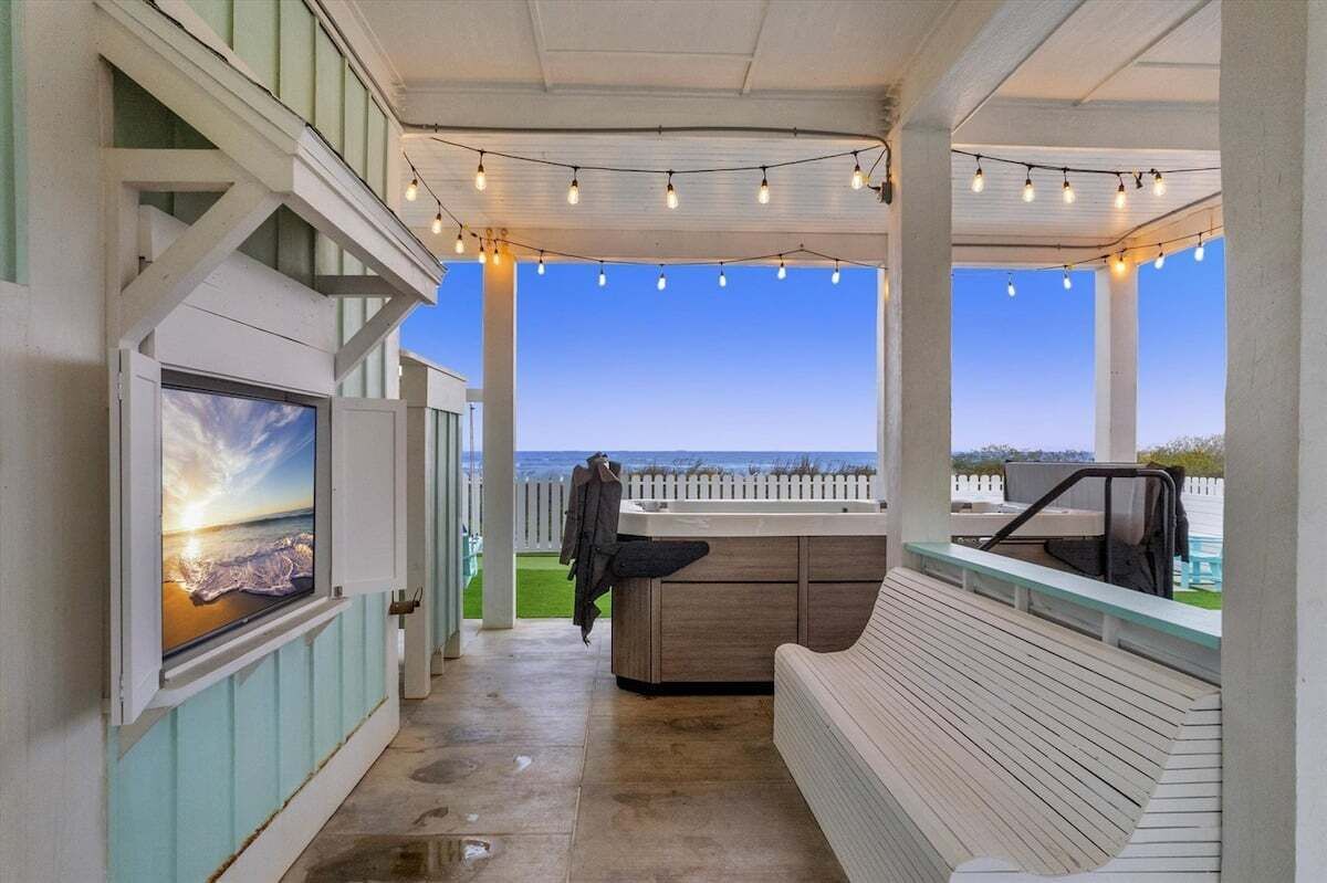A covered outdoor area with a wooden bench, a hot tub, and string lights.