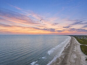 A coastal landscape with a beach, ocean, and a distant shoreline with buildings. - Beachfront Retreat with SwimSpa | Putt-Putt | Fire Pit | Sleeps 16 (Bolivar Peninsula)