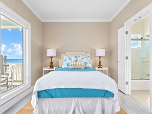 A bedroom with a bed, two bedside tables, a nightstand, a balcony with a view of the sea, and a glass shower door. - Beachfront Retreat with SwimSpa | Putt-Putt | Fire Pit | Sleeps 16 (Bolivar Peninsula)