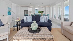 Un salon spacieux avec un canapé bleu foncé, une table basse en osier et une vue sur l’océan grâce à de grandes fenêtres.