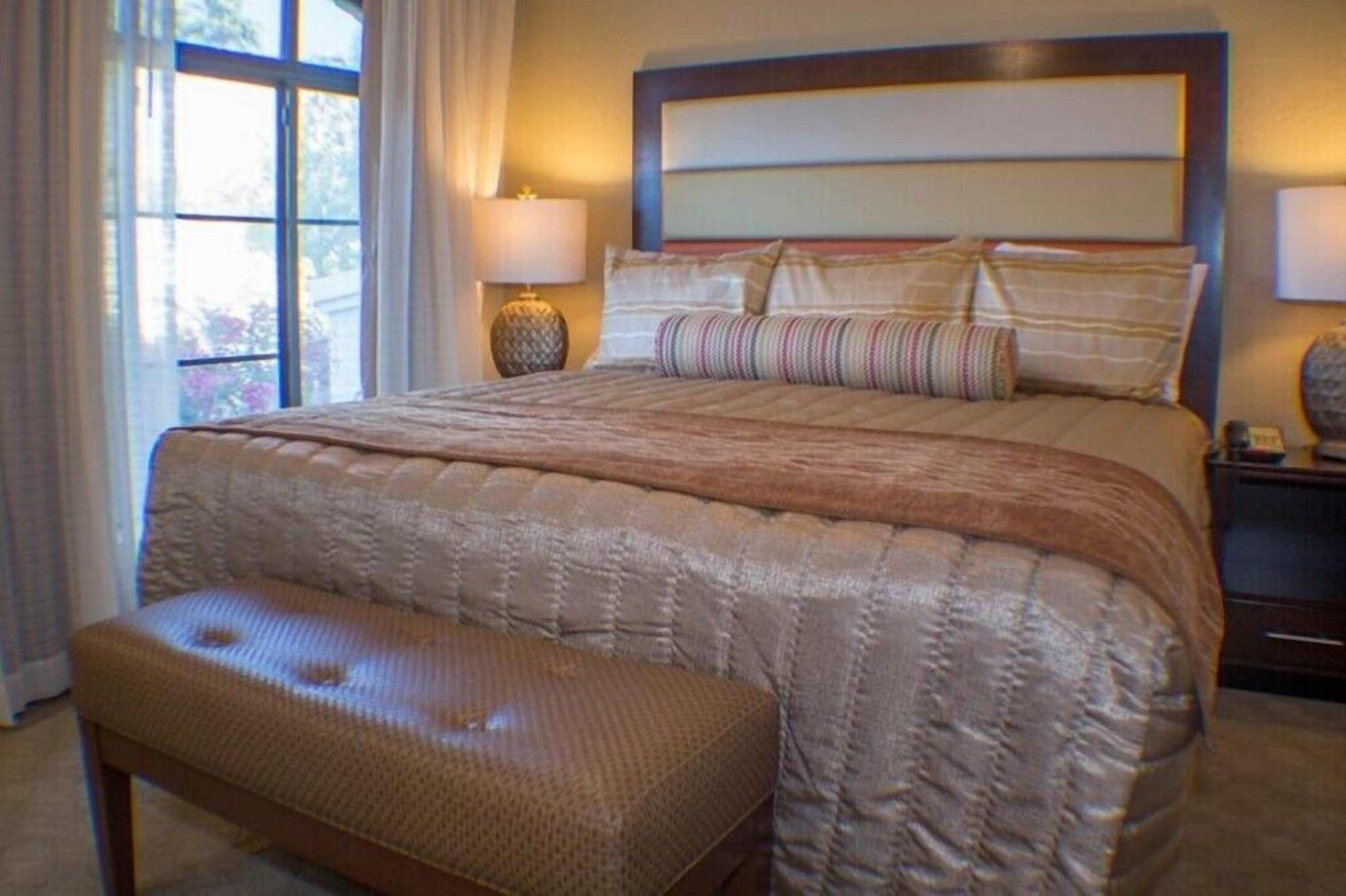 Ein Schlafzimmer mit einem großen Bett, einer Bank, einem Nachttisch und einem Fenster mit Vorhängen.