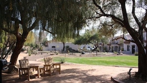 An outdoor patio area with wooden chairs and a table, surrounded by trees and a landscaped garden.