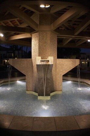 Una fuente nocturna con una estructura central de piedra y múltiples chorros de agua.