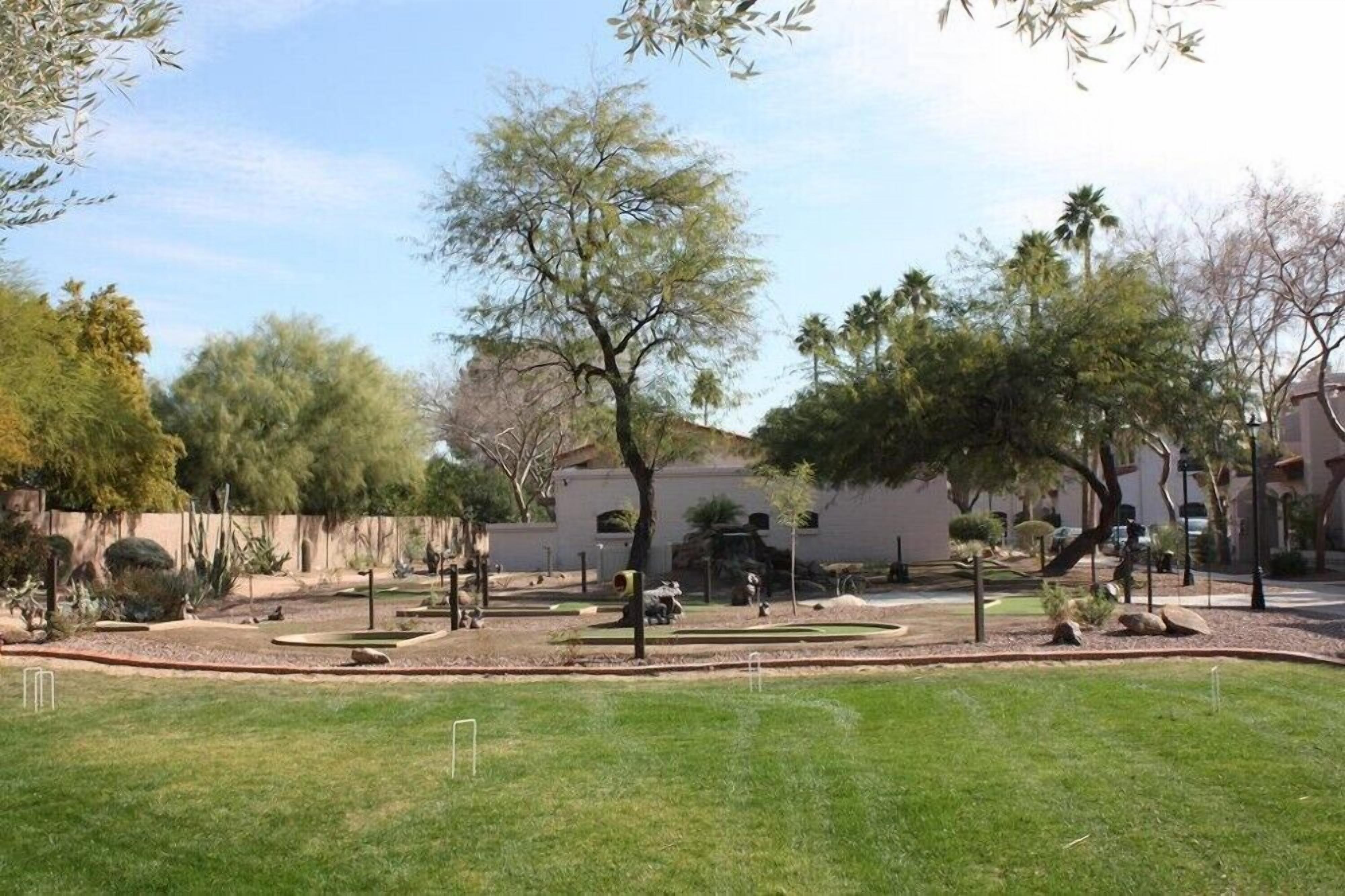 A landscaped outdoor area with a lawn, trees, and a white building in the background.