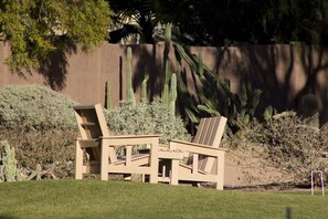 Dos sillas Adirondack de madera en un jardín, con un cactus y una valla de madera al fondo.