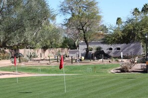 Un campo de golf con un césped bien cuidado, un edificio de piedra al fondo y una bandera al frente.