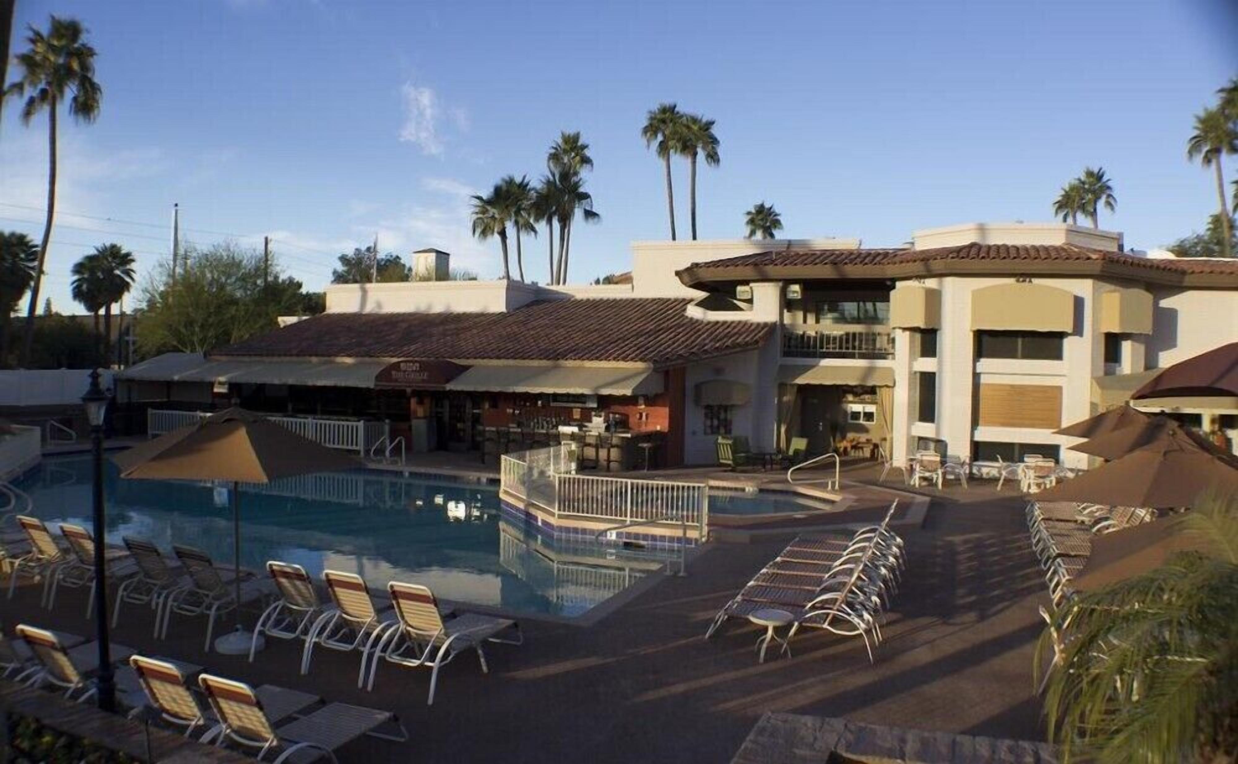A resort with a swimming pool, lounge chairs, and palm trees.