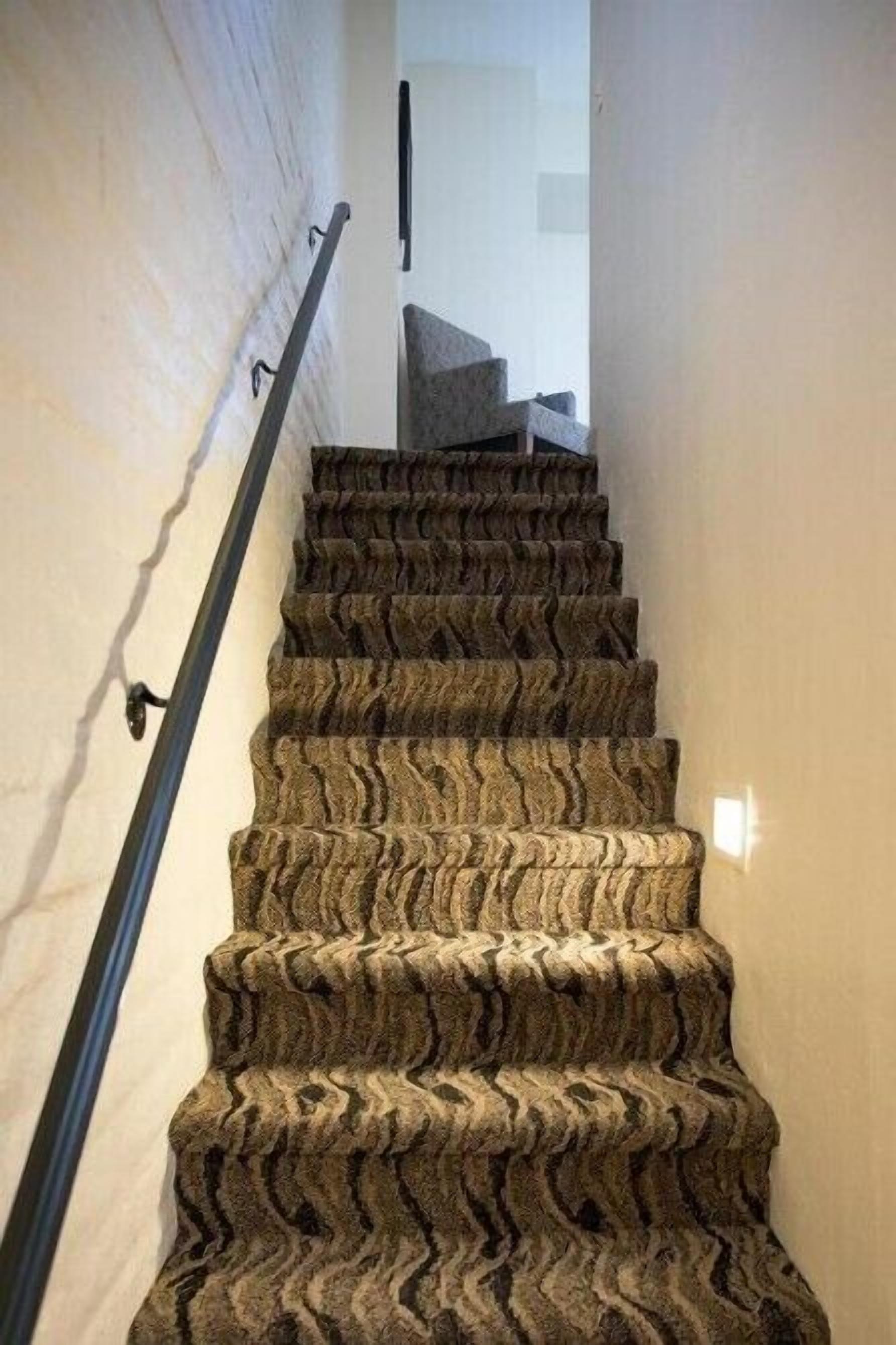 A carpeted staircase with a textured pattern, leading to a landing with a modern light fixture.