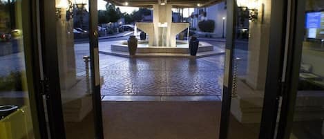 A hotel entrance with a central fountain, glass doors, and a tiled floor.