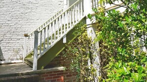 A white building with a brick base, a white staircase, and a balcony with white railings.