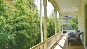 A wooden porch with white balustrades, two wicker chairs, and a view of dense green foliage.