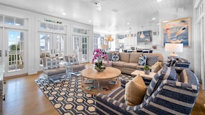 A spacious living room with a large sofa, a coffee table, and a dining area with a kitchen in the background. - Gulf Front Views | "All Decked Out" Luxurious WaterColor Home | Steps to the Beach Club (Santa Rosa Beach)