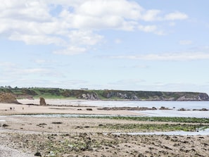 A coastal landscape with a sandy beach, rocky outcrops, and a grassy cliff.