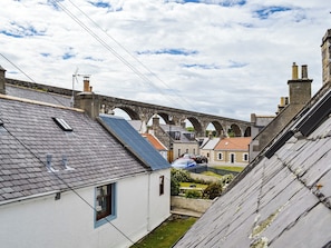 A narrow street with a stone bridge, white buildings, and a small garden.