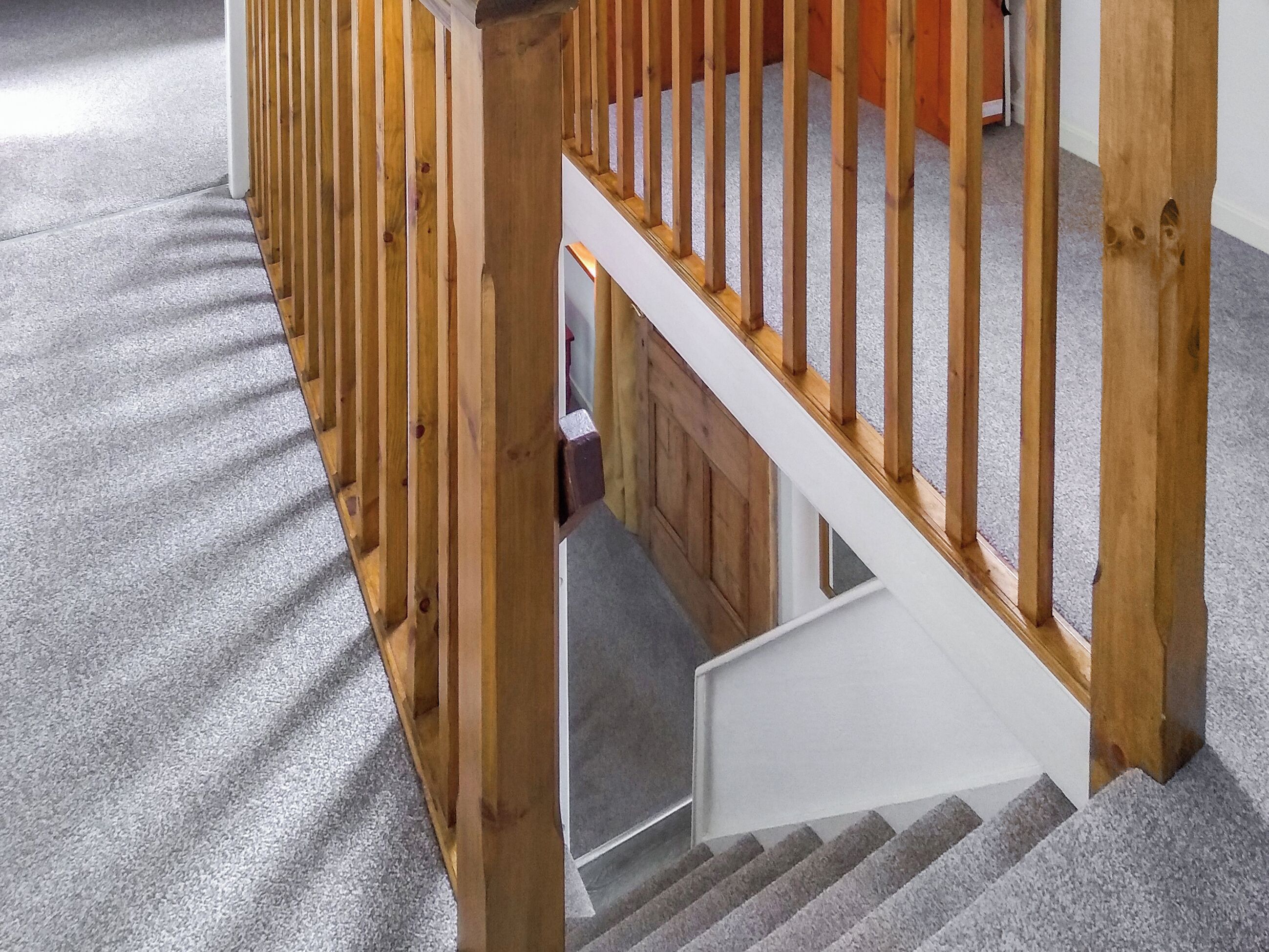 Una escalera de madera con piso alfombrado que baja a un nivel inferior.