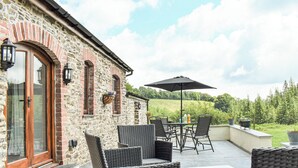 A patio with wicker furniture, a table, and an umbrella. - Slade Cottage - UK35027 (Brayford)