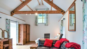 A spacious room with a wooden ceiling, a leather sofa with red cushions, a wooden table, and a bed with floral curtains. - Slade Cottage - UK35027 (Brayford)