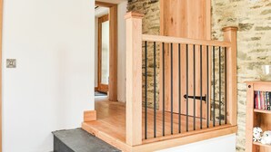 A wooden staircase with a metal railing leading to a room with a stone wall. - Slade Cottage - UK35027 (Brayford)