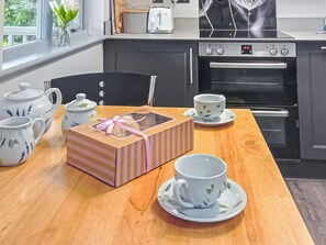 Una cocina con una mesa de madera, un juego de té, una caja de pastel y un tostador.
