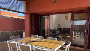 A patio with a wooden table and white chairs, a sofa, and a glass door leading to an indoor living area. - Large villa with private heated pool (Corralejo)