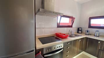 A modern kitchen with stainless steel appliances, a window above the sink, and a red dish rack.