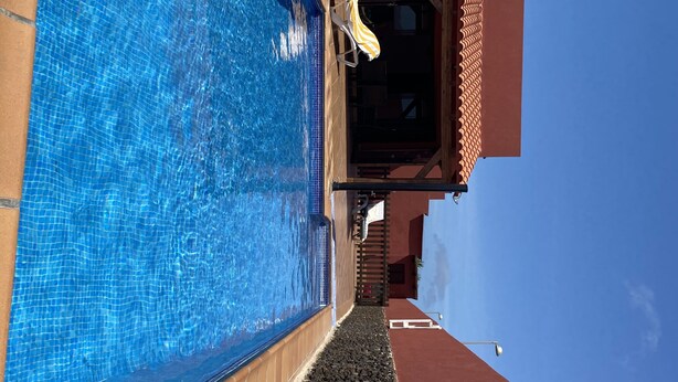 A swimming pool with clear blue water, a wooden deck, and a tiled roof structure. - Large villa with private heated pool (Corralejo)