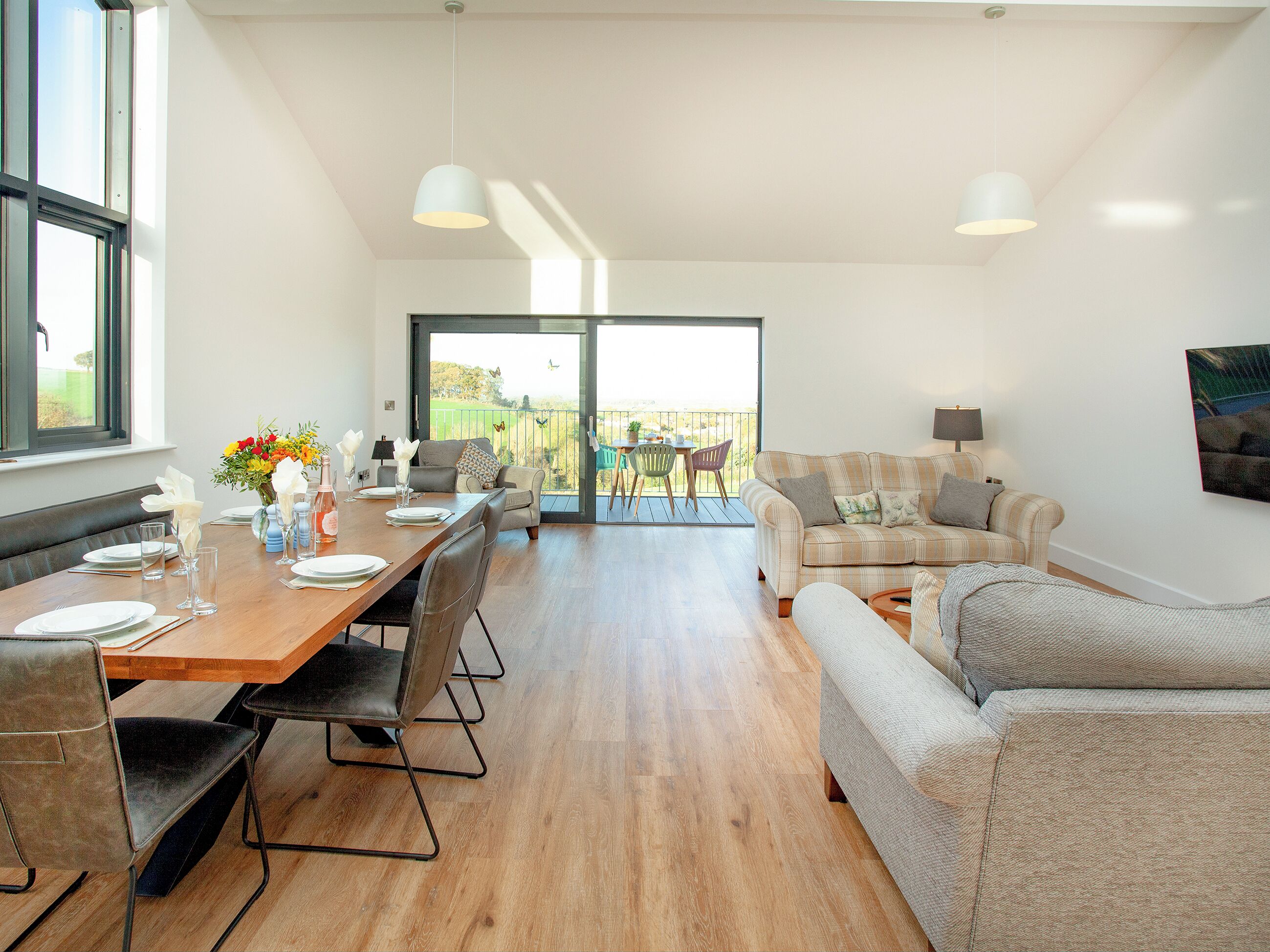 Een moderne woonkamer met een eethoek, grote ramen en een balkon met stoelen.
