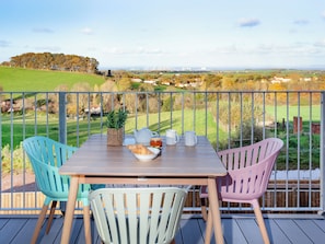 A wooden table with chairs on a balcony overlooking a rural landscape.